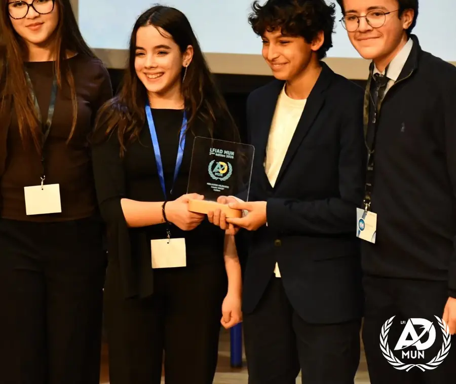Quatre élèves en tenue de cérémonie ; l'une tient un trophée en verre