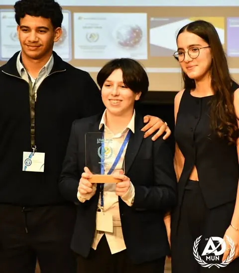 Trois élèves posent ensemble, l'une tient un trophée en verre