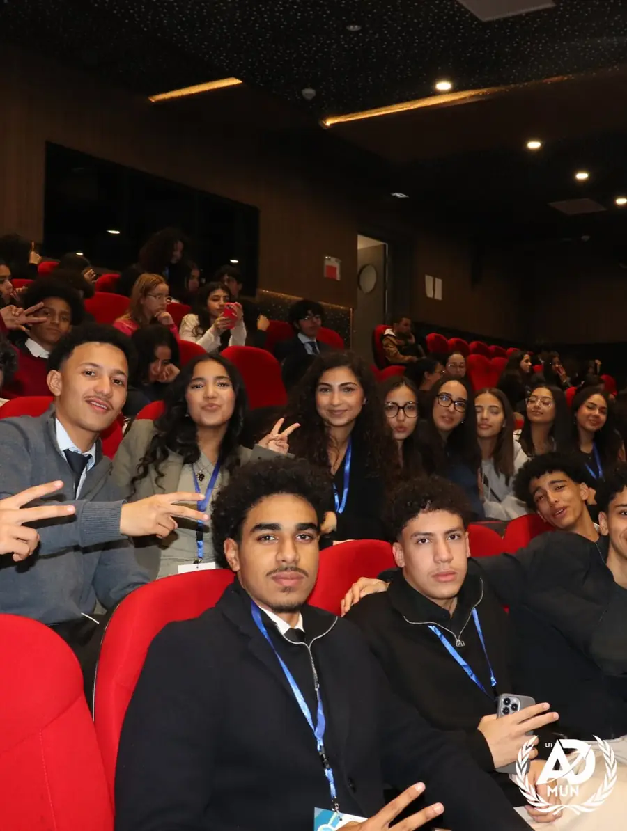 Des élèves délégués souriants, badge autour du cou, assis dans les fauteuils rouges de la salle