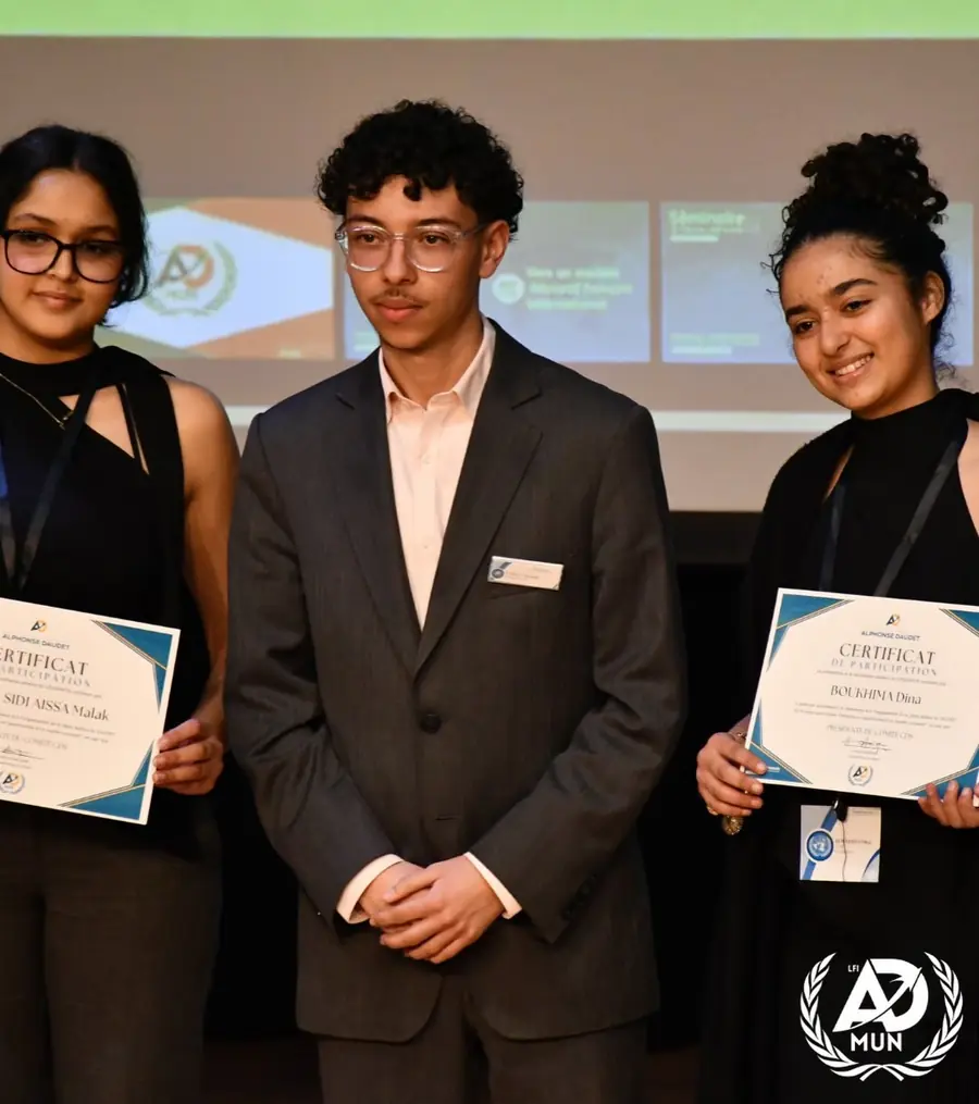 Un délégué en costume entouré de deux élèves qui tiennent leur certificat